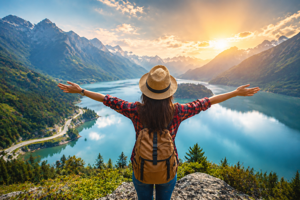 Traveler standing with open arms enjoying scenic mountain lake view during sunrise travel adventure